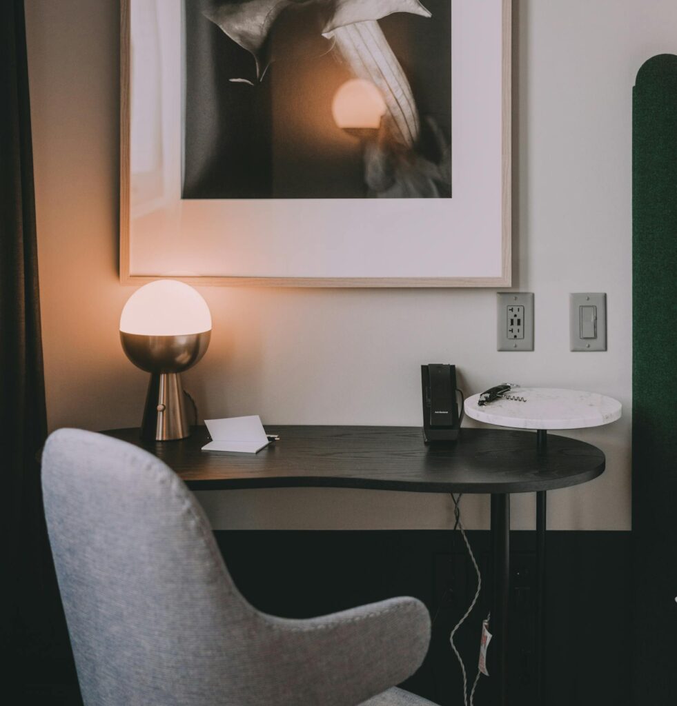 Soft armchair against table with shiny lamp reflecting in photography on wall in house