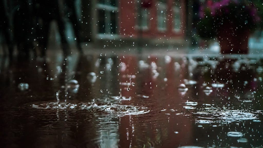 Close-up of raindrops splashing into a puddle, capturing reflections and textures in an outdoor urban setting.